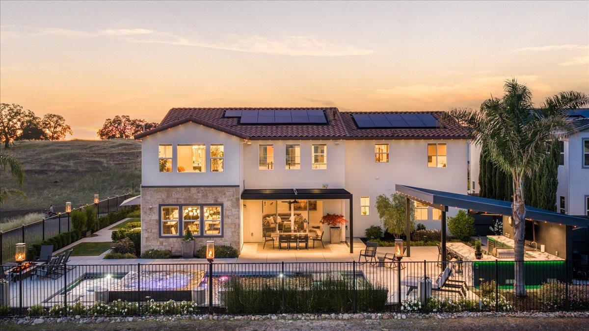 Two-story home with rooftop solar panels, a backyard pool, and a covered patio at dusk.