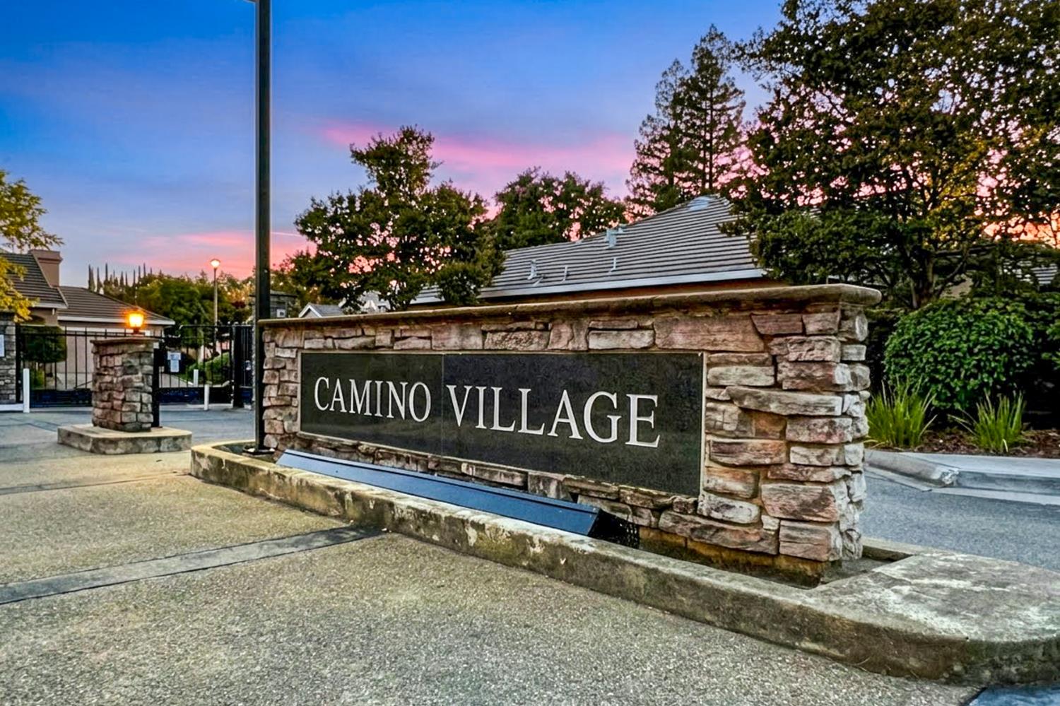 Camino Village stone entrance sign beneath a pink and blue dusk sky.