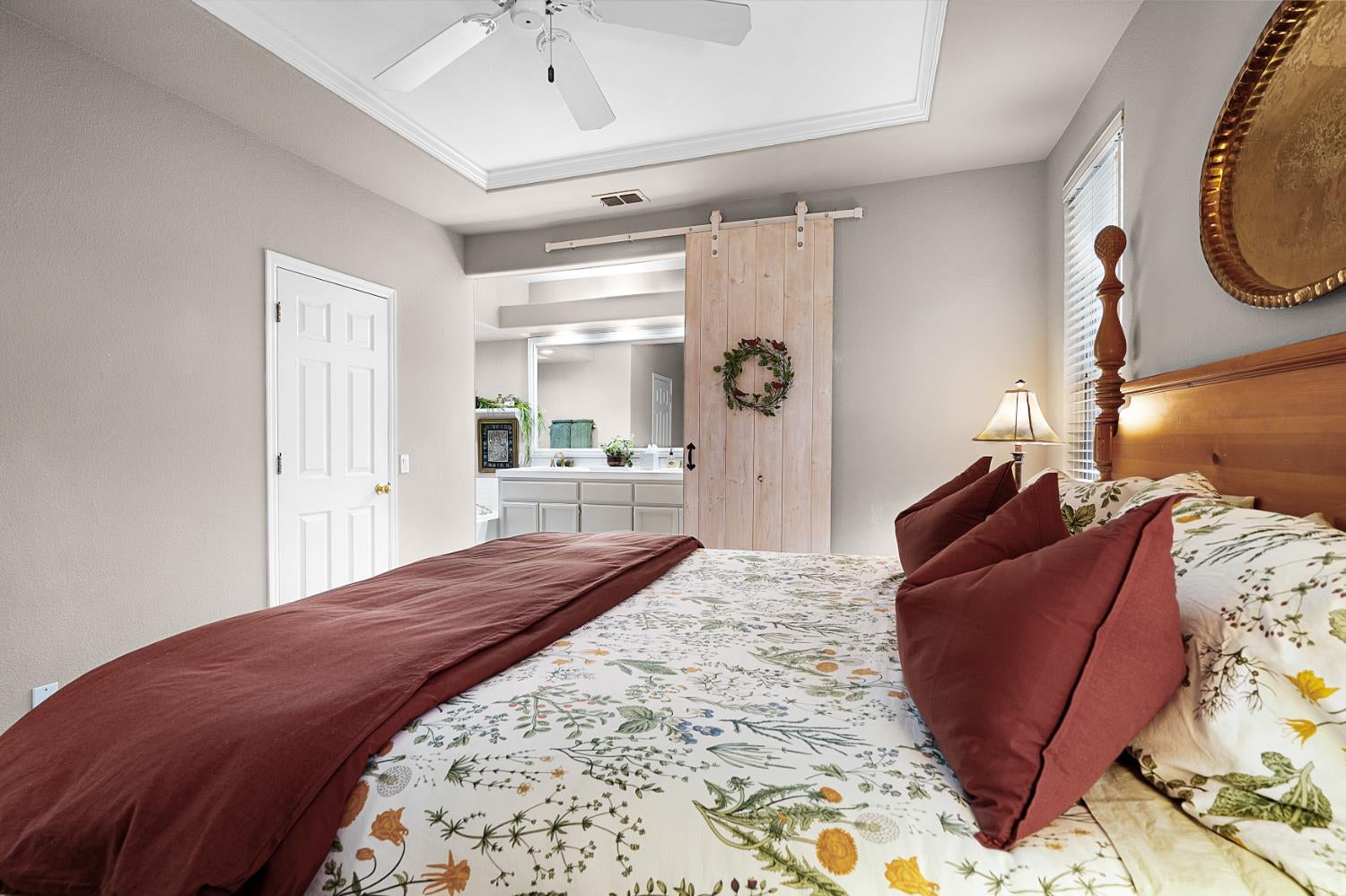 Bedroom with floral bedding, burgundy pillows, and a sliding barn door to the bathroom.