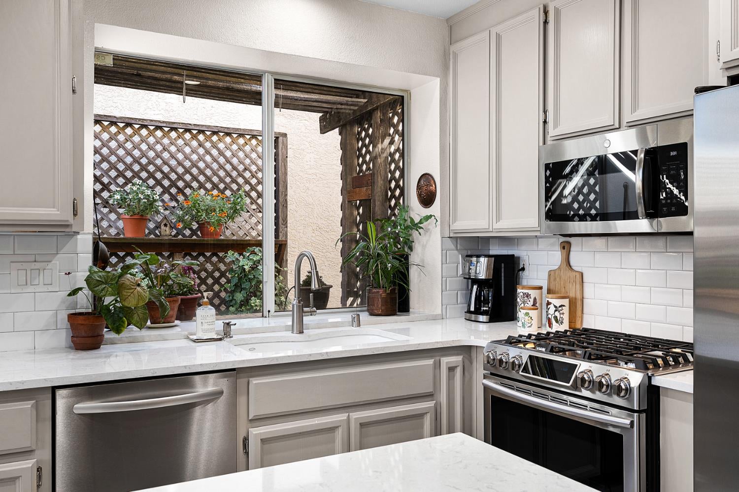 Kitchen with stainless steel appliances and a large window overlooking a plant-filled patio.