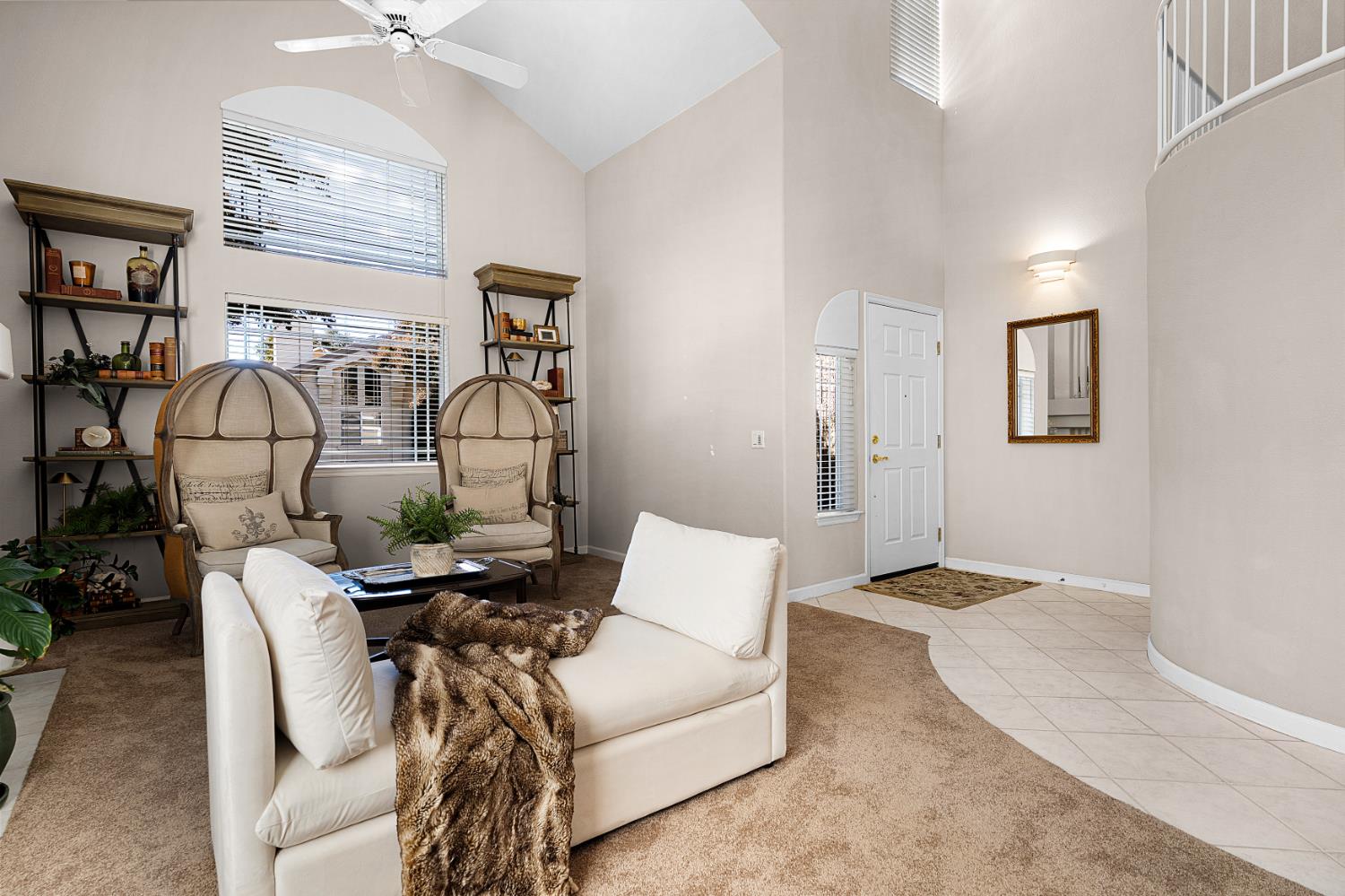 Living room with vaulted ceiling, tall windows, cream seating, and curved upstairs railing.