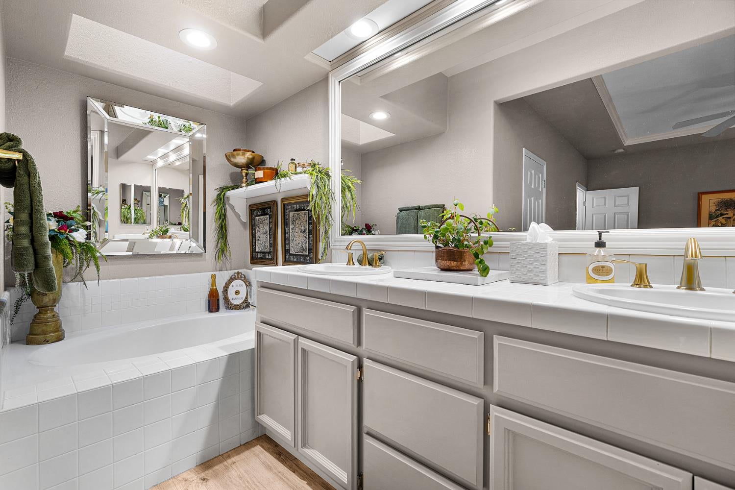 Bathroom with a tiled bathtub, double vanity, large mirrors, and brass faucets.