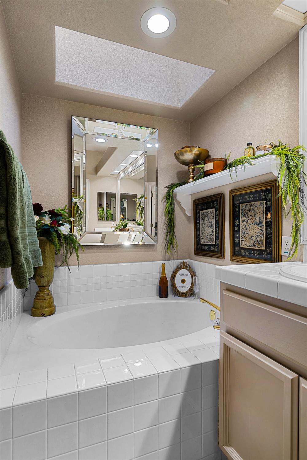 Bathroom soaking tub beneath a skylight, with a mirrored wall and decorative plants.