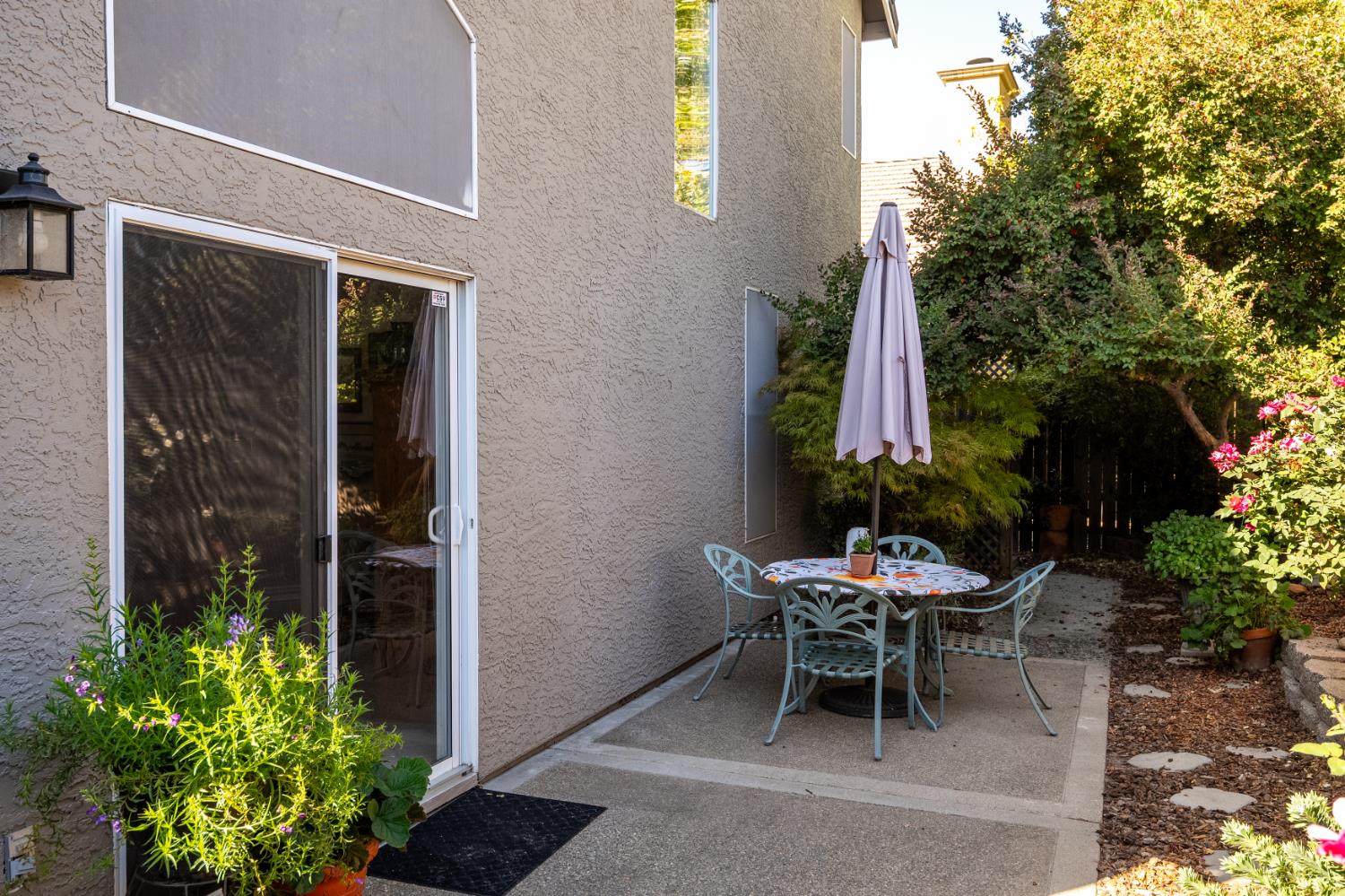 Outdoor patio with a round table, metal chairs, closed umbrella, and sliding glass door.