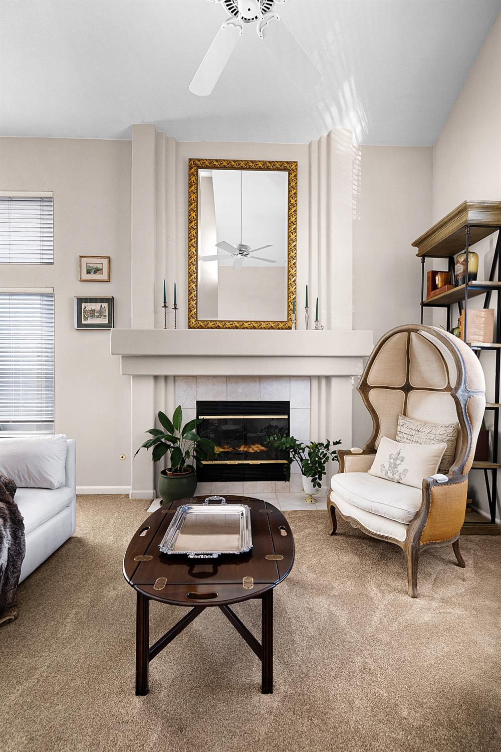 Living room with a tall fireplace, ornate gold-framed mirror, and upholstered armchair.