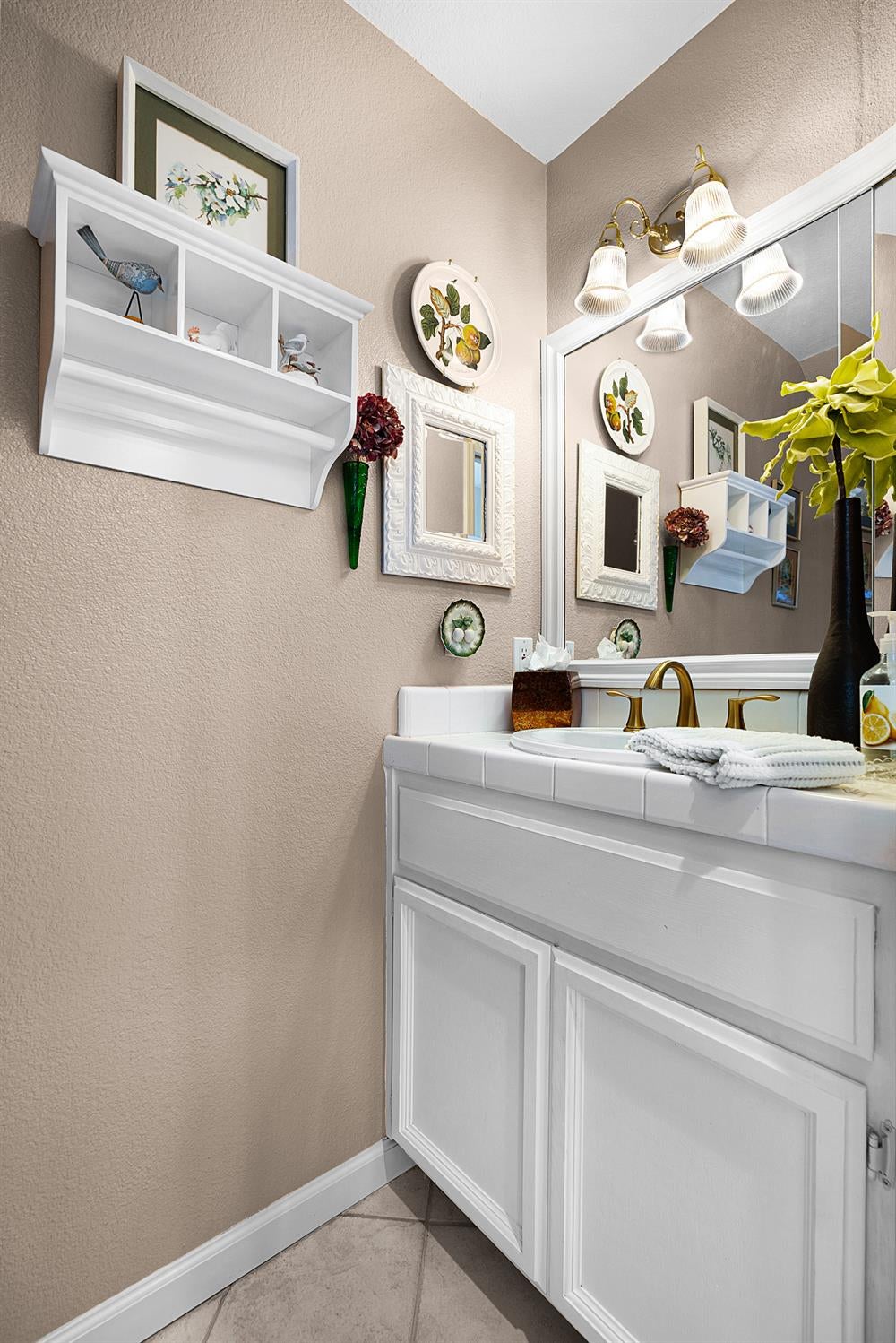 Bathroom vanity with a brass faucet, large mirror, and white paneled cabinetry.