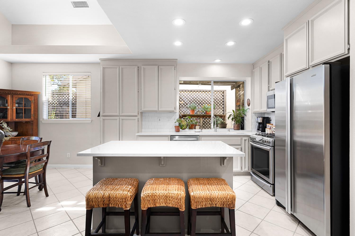 Kitchen with a large island, stainless steel appliances, and three woven stools.