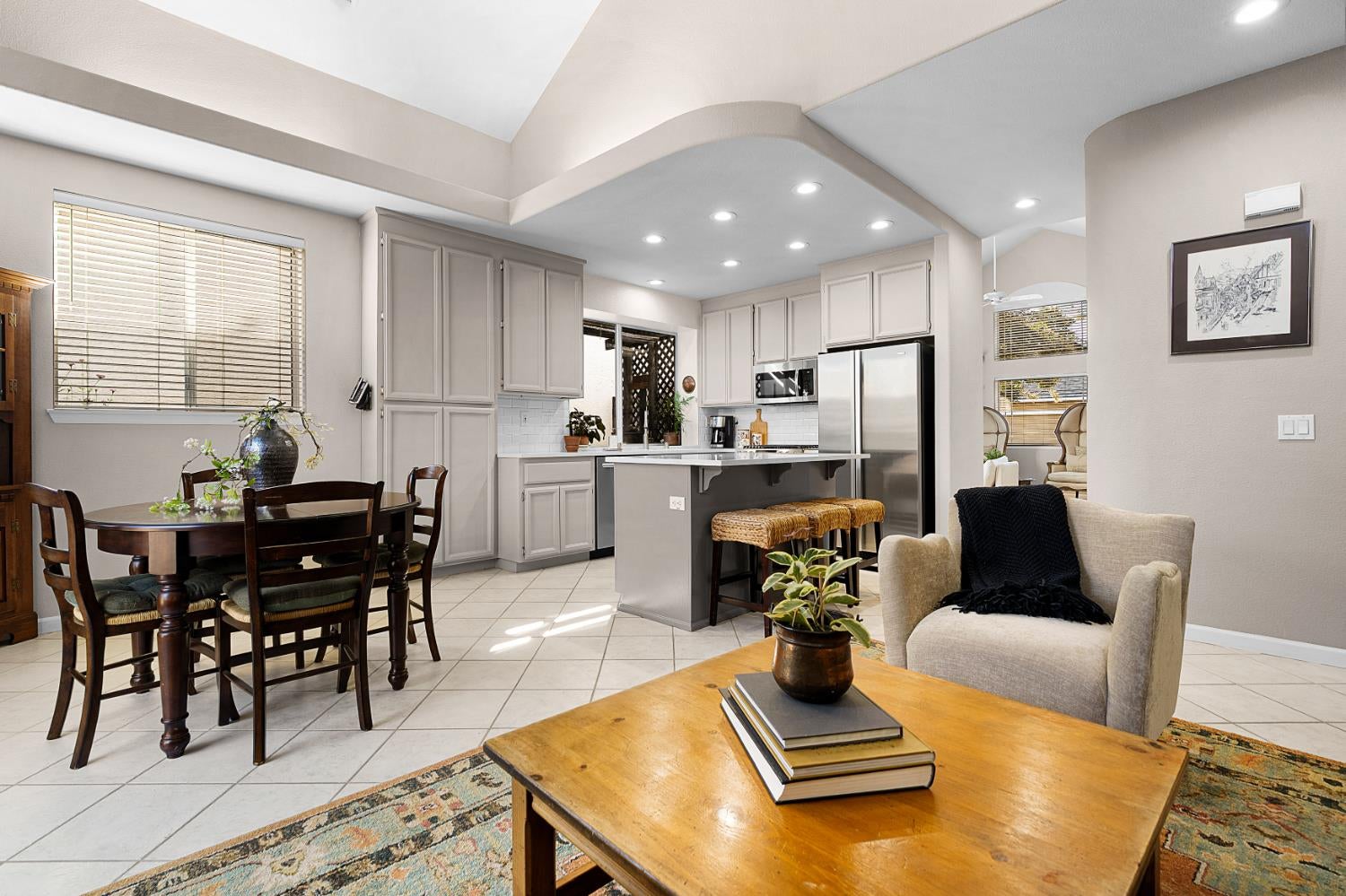 Open-plan kitchen with gray island and stainless appliances beside a round dining table.