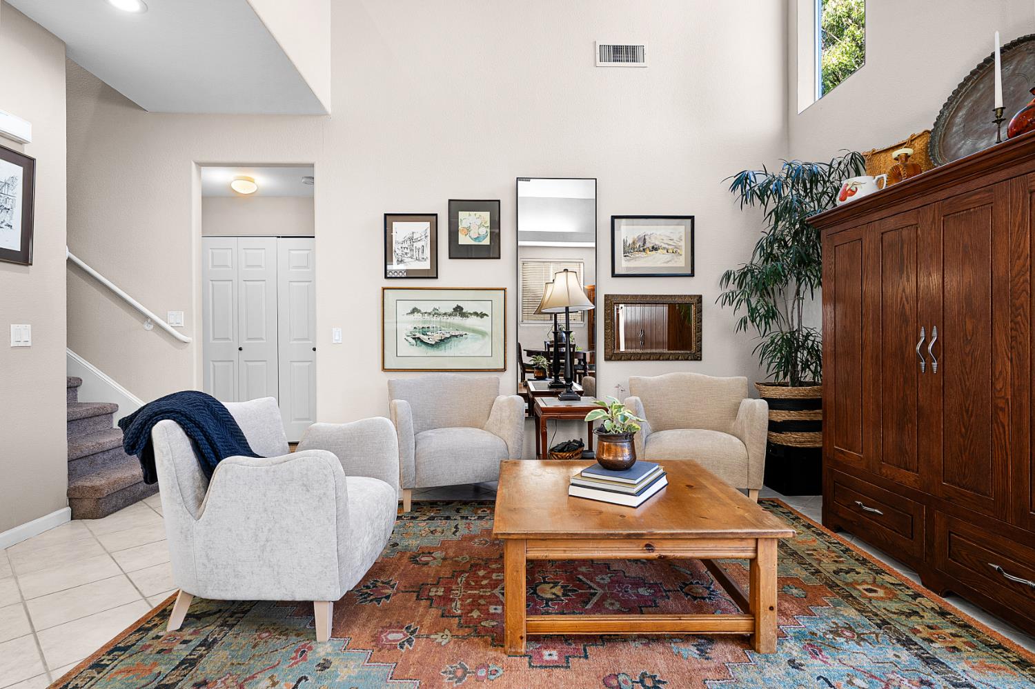 Living room with a vaulted ceiling, pale armchairs, patterned rug, and large wooden cabinet.