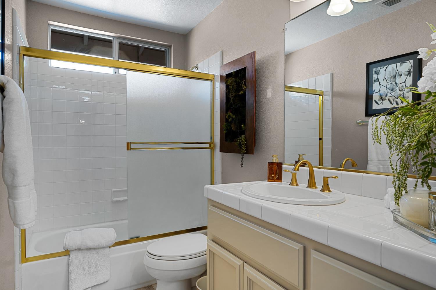 Bathroom with gold-trimmed frosted shower doors and a cream vanity with a gold faucet.