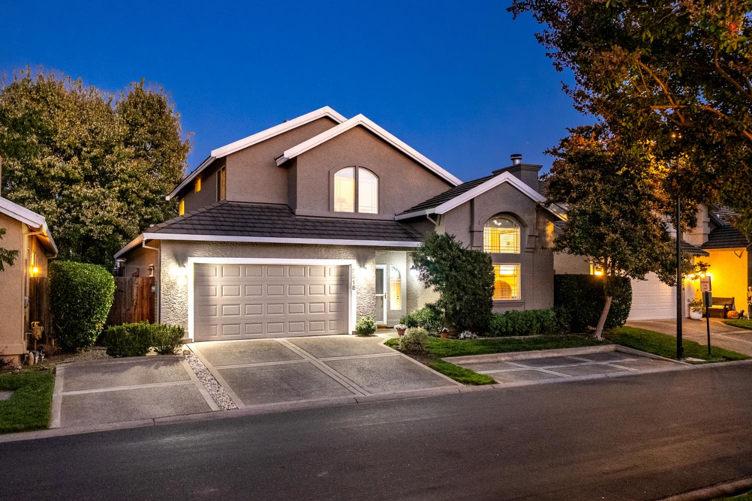Two-story gray home with a double garage, arched windows, and illuminated landscaping at dusk.