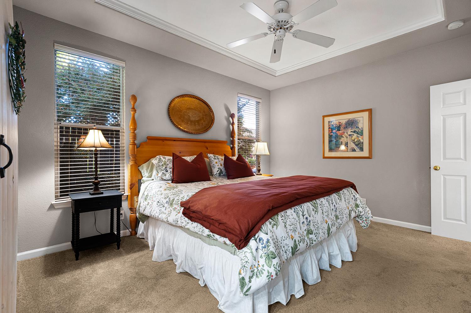 Bedroom with a four-poster bed, floral bedding, burgundy accents, and two windows with blinds.