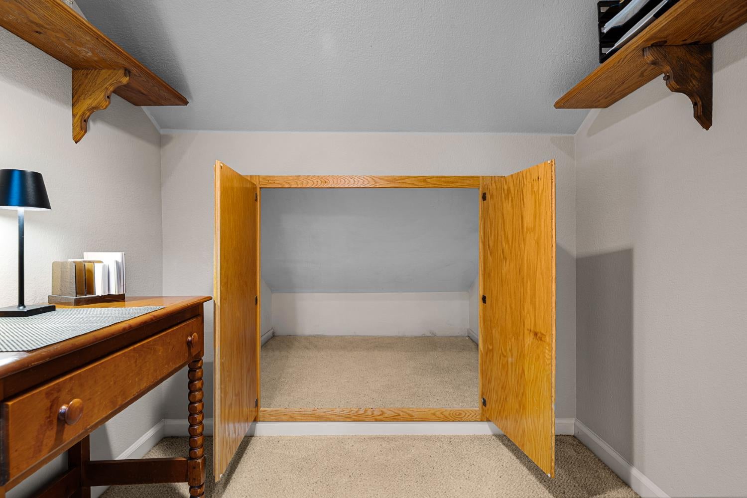 Carpeted closet with open wooden double doors, high shelves, and a small desk.