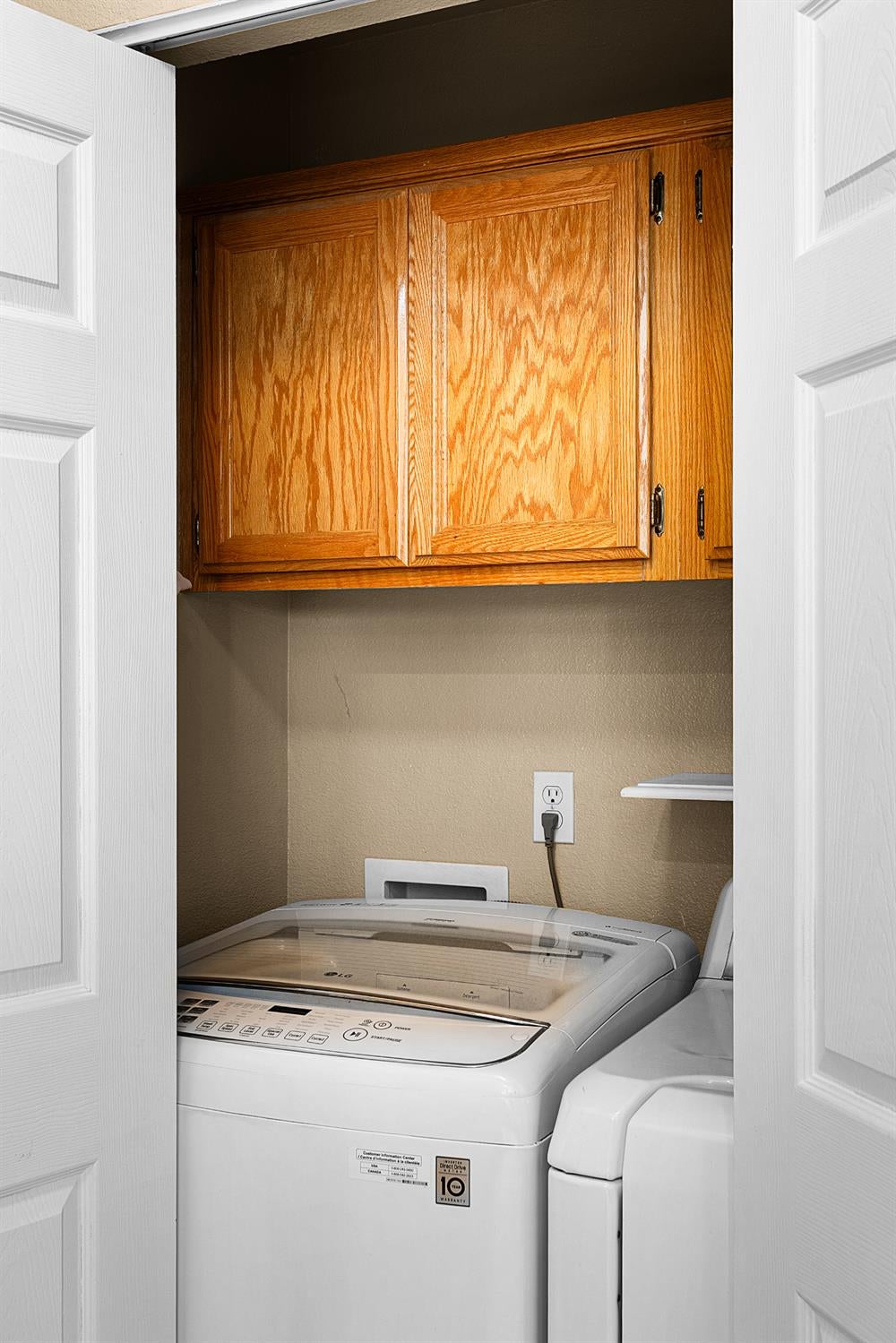 Laundry closet with a top-loading washer and dryer beneath warm wood cabinets.