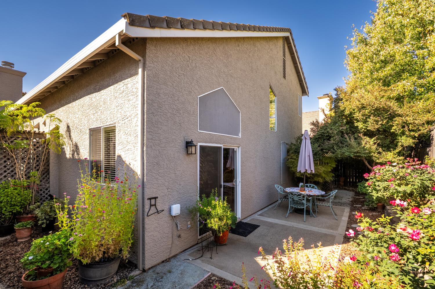 Two-story stucco home with a patio dining set and flowering garden beds.