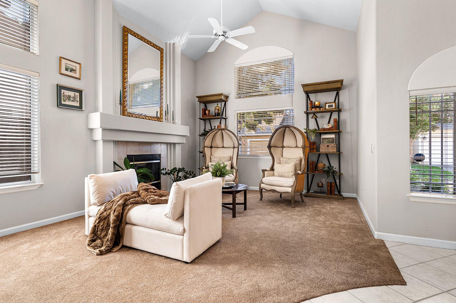 Living room with a vaulted ceiling, fireplace, and two tall upholstered chairs beside large windows.