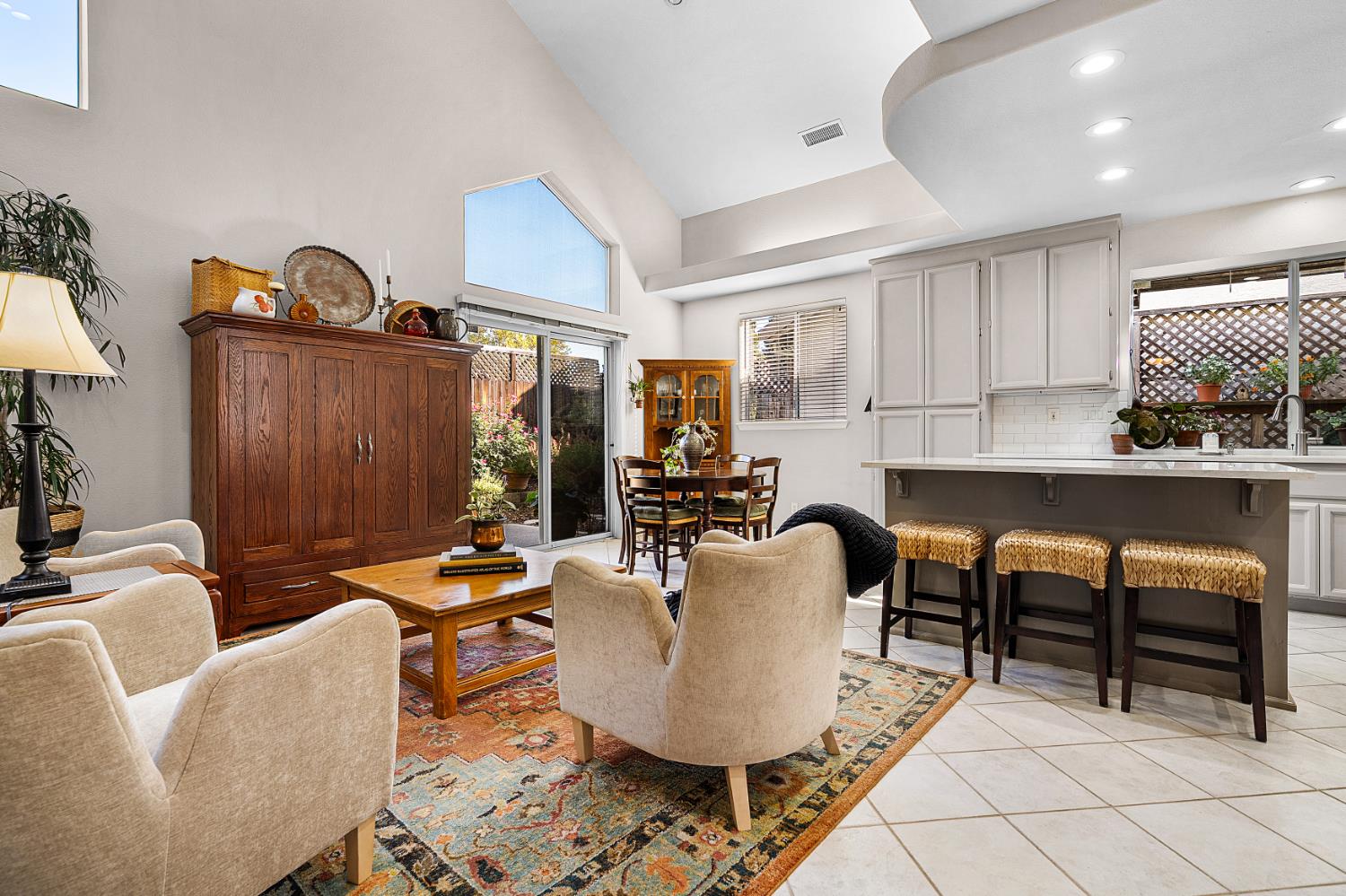 Open-plan living room with vaulted ceiling, colorful rug, dining nook, and kitchen breakfast bar.