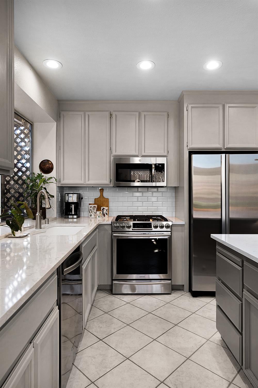 Kitchen with gray cabinets, white counters, stainless appliances, and a sink beneath a window.