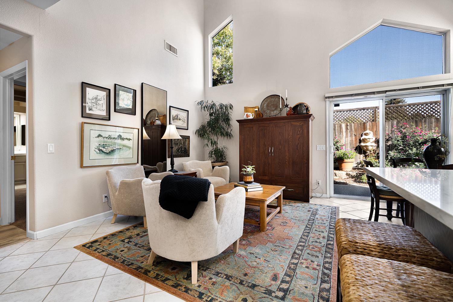 Vaulted living room with light armchairs, a patterned rug, and sliding doors opening to a garden patio.