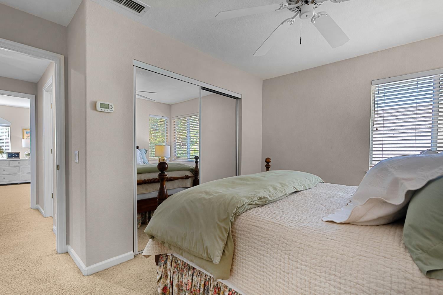 Bedroom with pale green bedding, mirrored closet doors, and a ceiling fan.