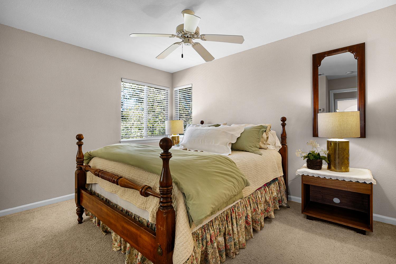 Bedroom with a dark wood four-poster bed, sage bedding, corner windows, and a ceiling fan.