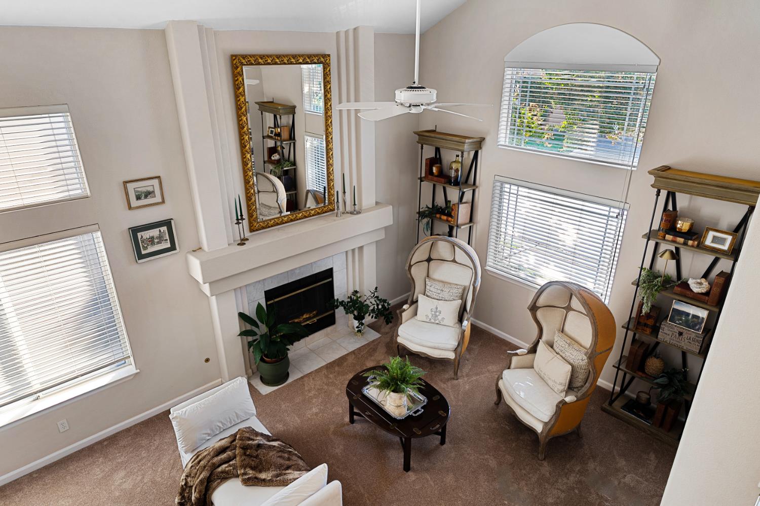 Living room with a fireplace, tall windows, and upholstered chairs arranged around a coffee table.