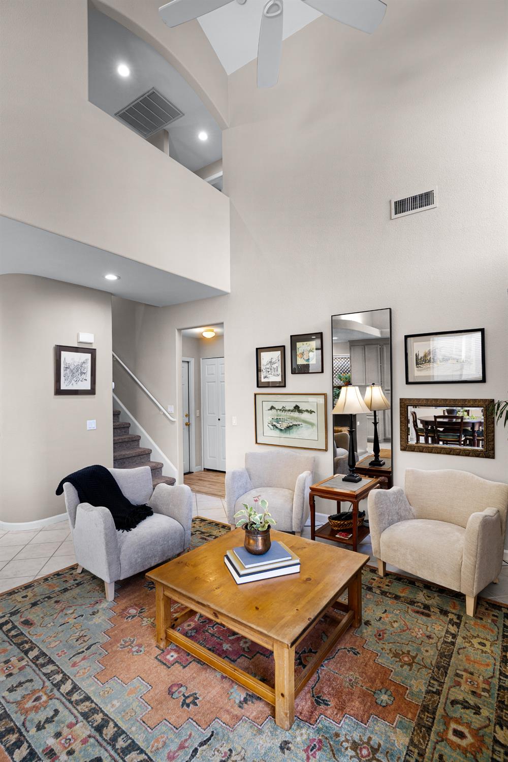 Living room with vaulted ceiling, upstairs overlook, staircase, and seating around a wooden coffee table.