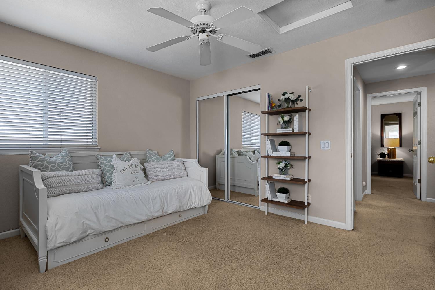 Staged bedroom with a white daybed, mirrored closet doors, and open shelving.