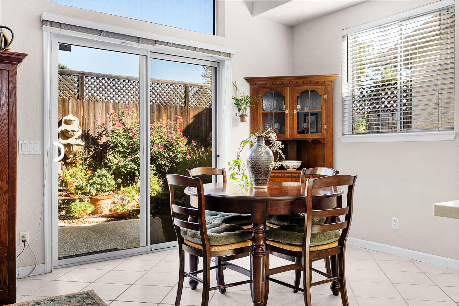 Dining room with a round wood table beside sliding glass doors overlooking a flower-filled garden.