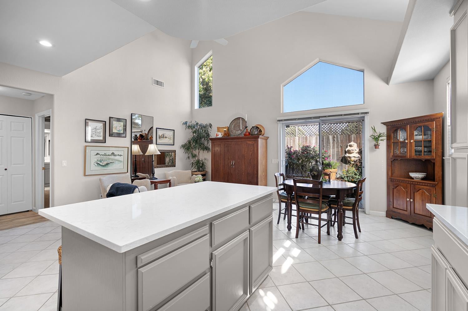 Kitchen and dining area with a large white island, vaulted ceiling, and garden-facing sliding doors.