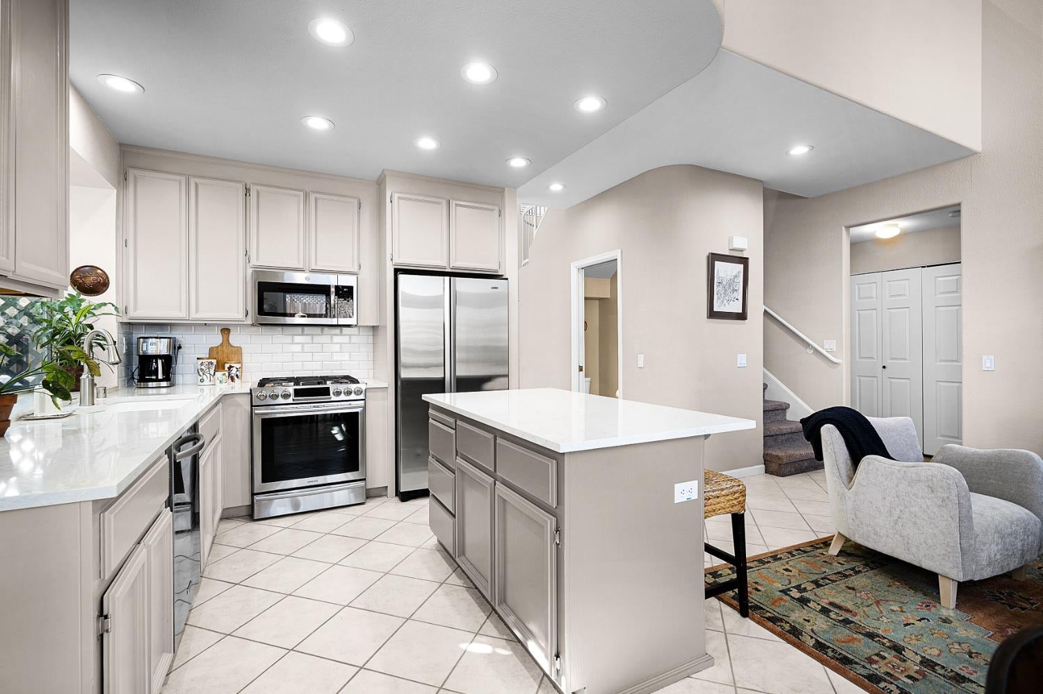 Kitchen with a large white island, light cabinetry, and stainless steel appliances beside a seating area.