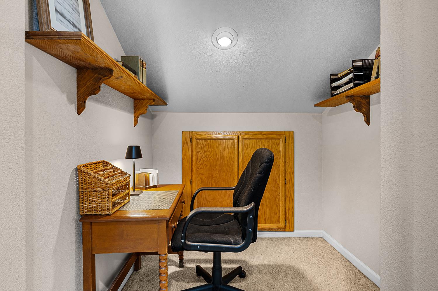Compact office nook with a wooden desk, black rolling chair, and shelves above.