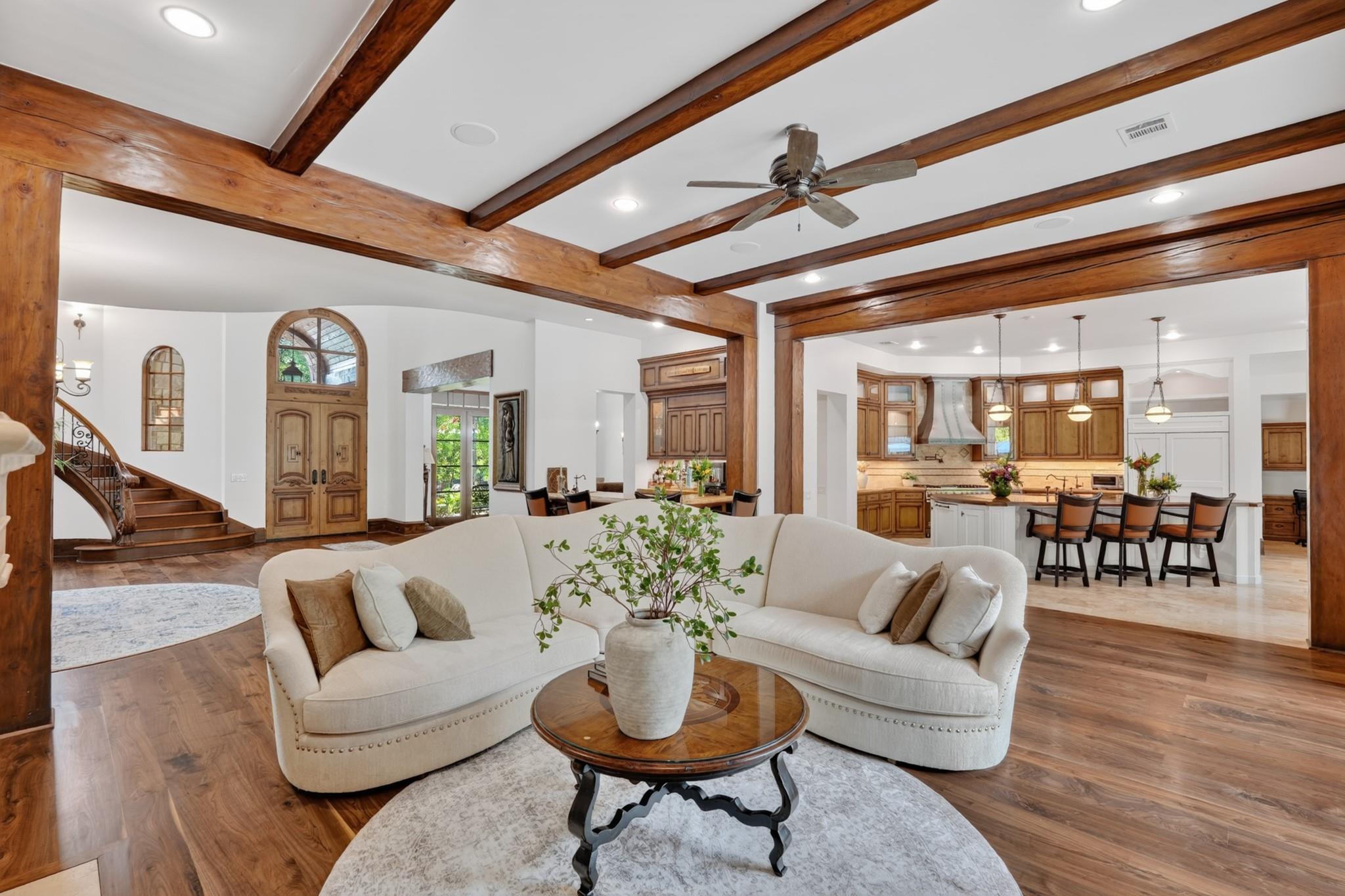 Open-plan living room with white sofas and exposed wood beams, leading to a kitchen with island seating.