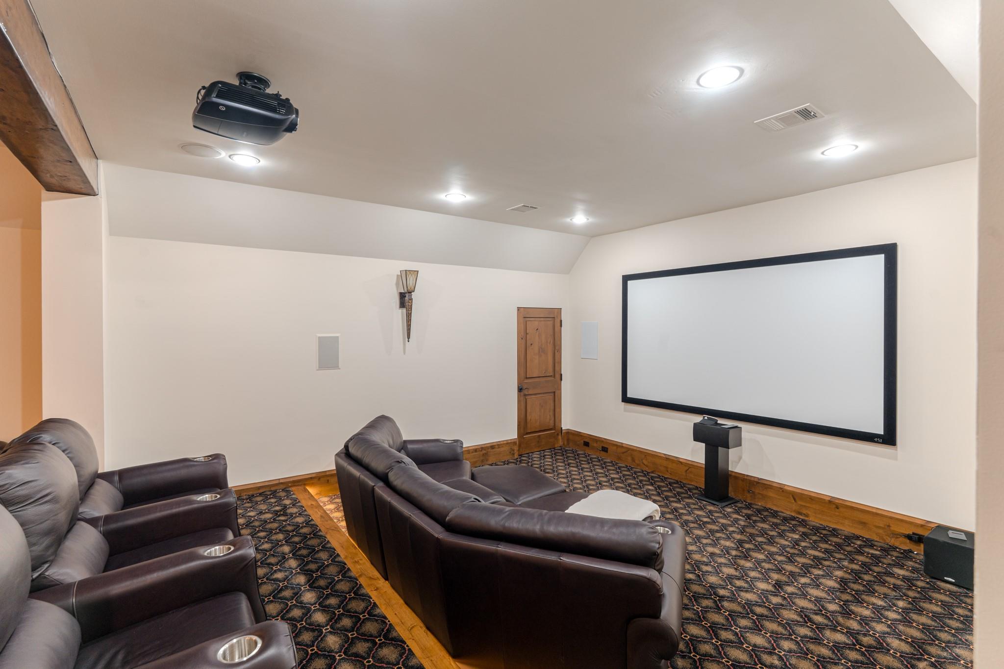Home theater with leather recliners, a large projection screen, and a ceiling-mounted projector.