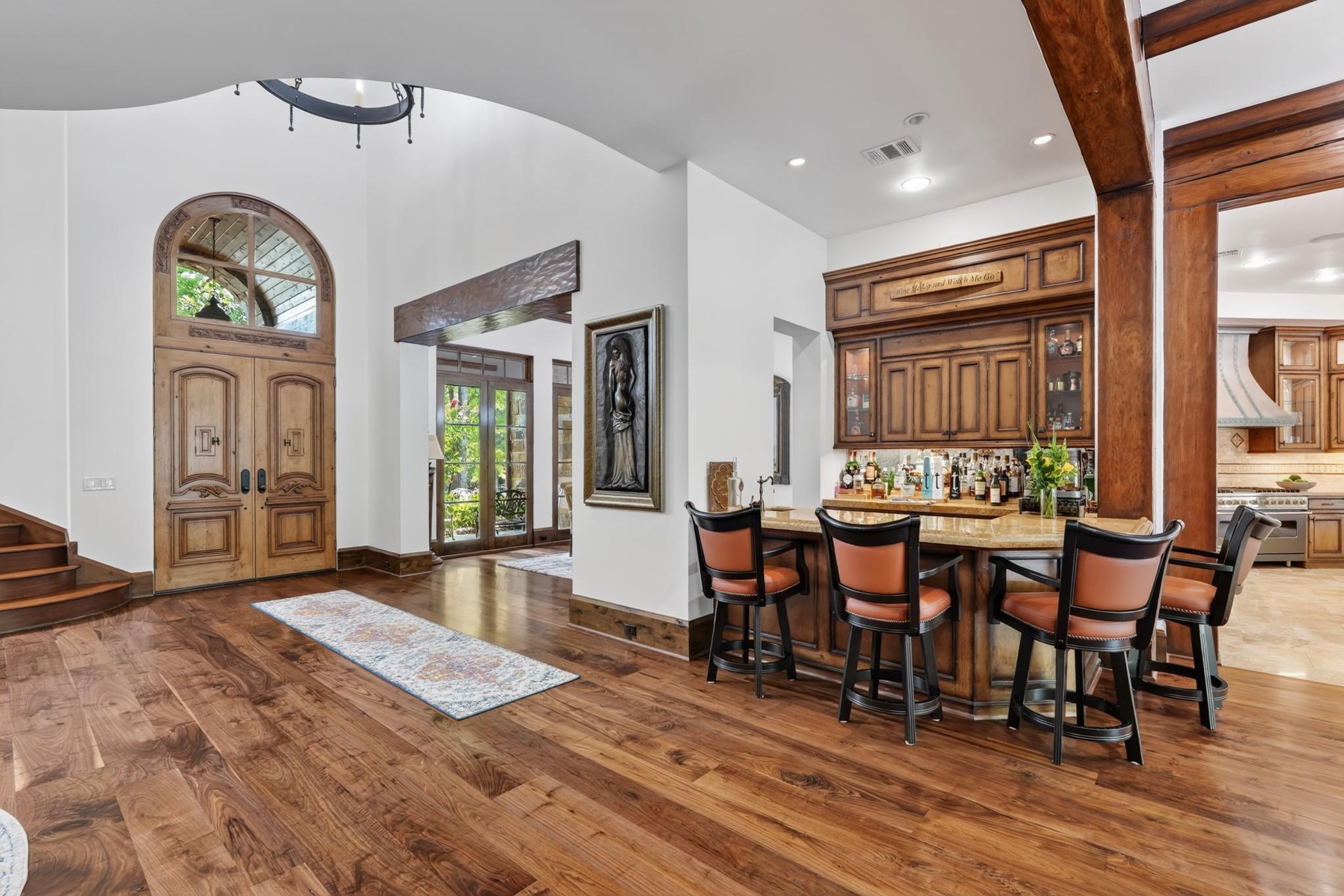 Entry foyer with an arched wood front door, hardwood floors, and a built-in bar with seating.