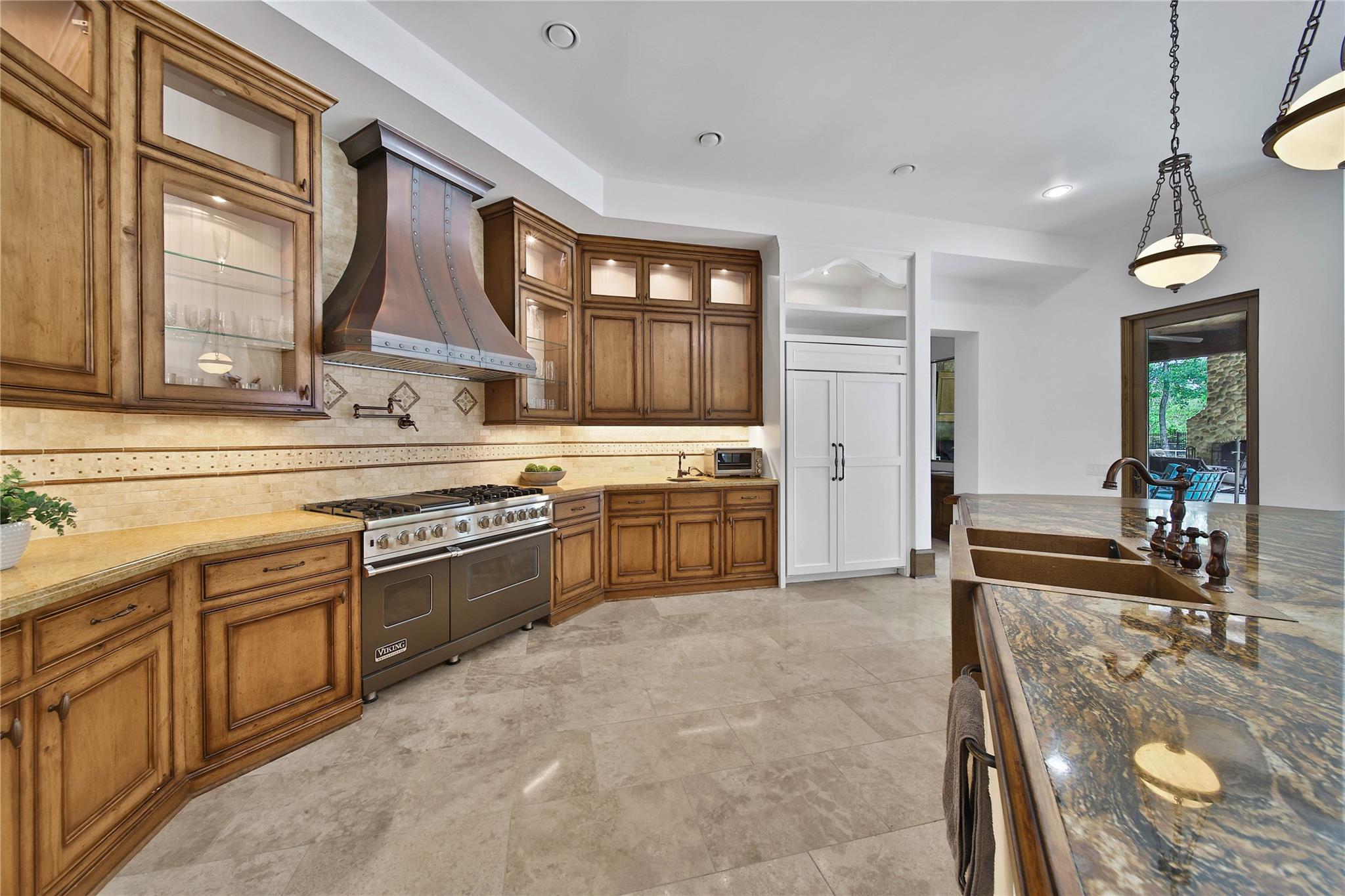 Kitchen with wood cabinets, a stainless range beneath a copper hood, and a granite island with a deep sink.
