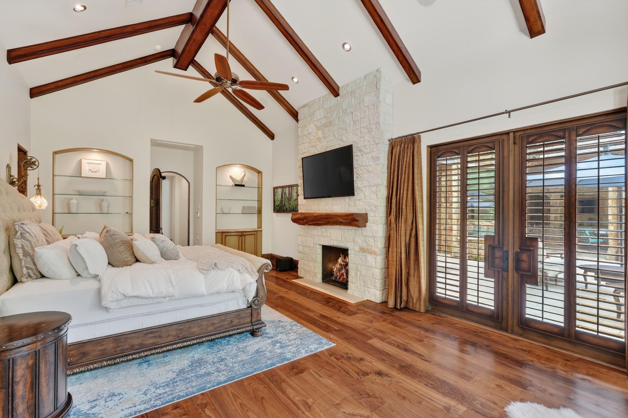 Bedroom with vaulted wood-beamed ceiling, stone fireplace, and plantation-shuttered doors.