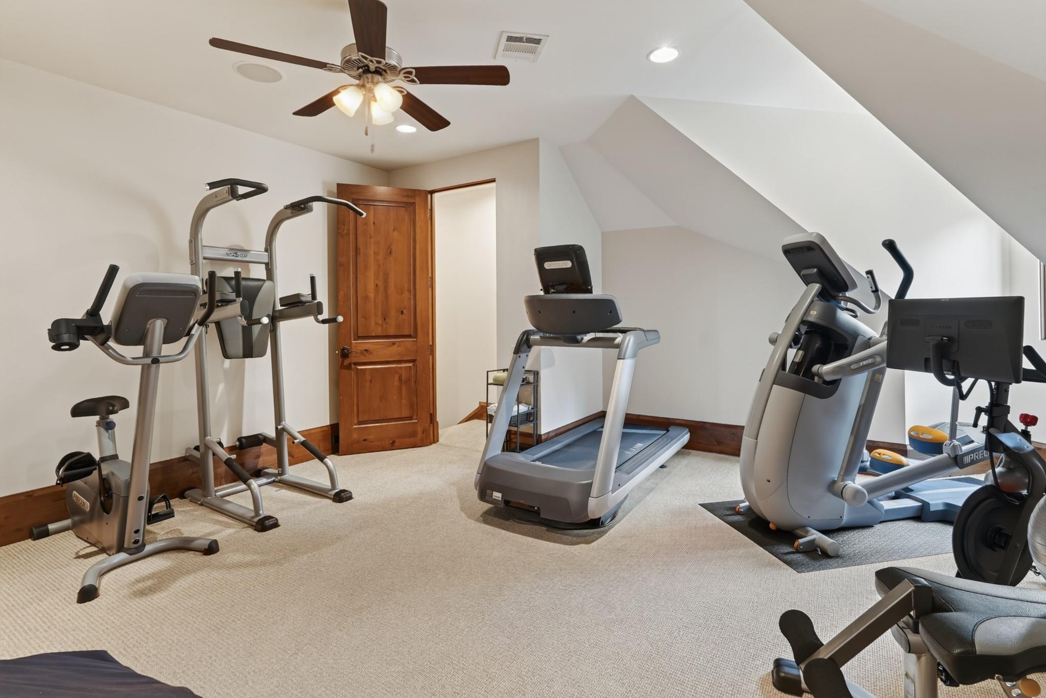 Home gym with a treadmill, elliptical machines, and strength-training equipment beneath a sloped ceiling.