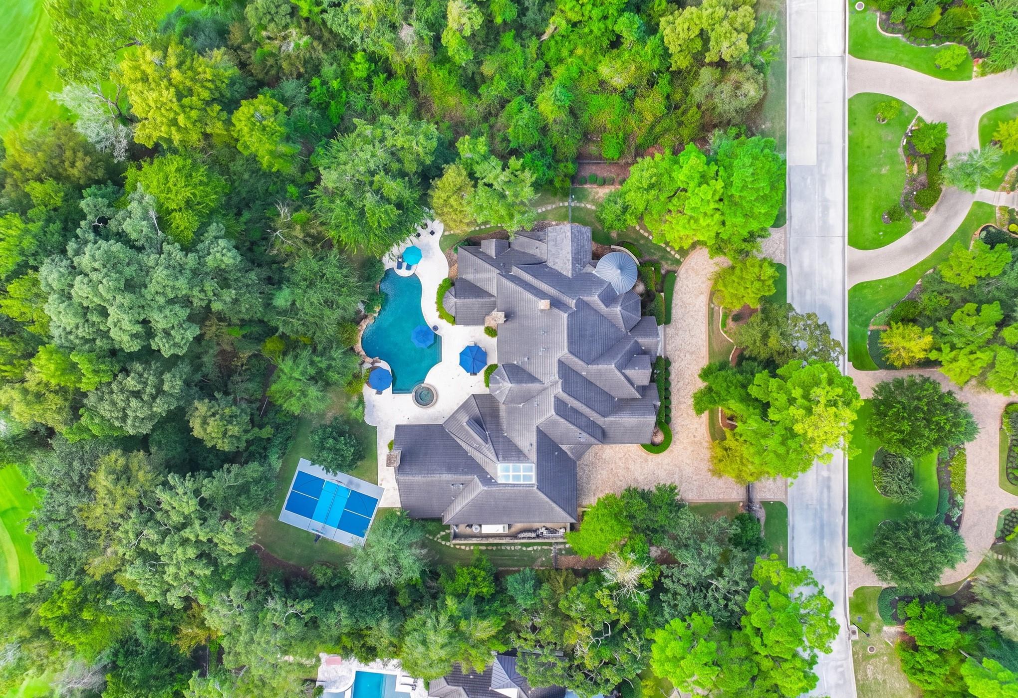 Aerial view of a large wooded property with a swimming pool, spa, and tennis court.