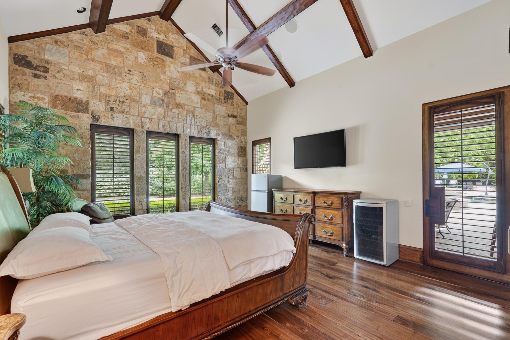 Bedroom with a stone accent wall, vaulted beamed ceiling, and large wooden bed.