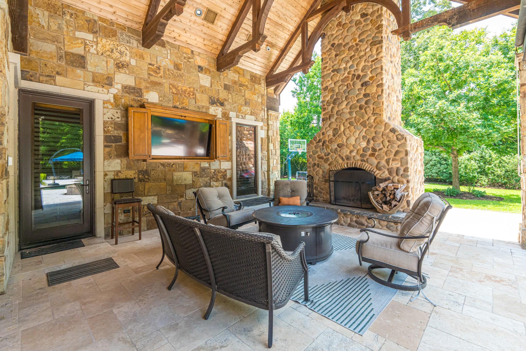 Covered stone patio with a massive river-rock fireplace, vaulted timber ceiling, and cushioned seating.