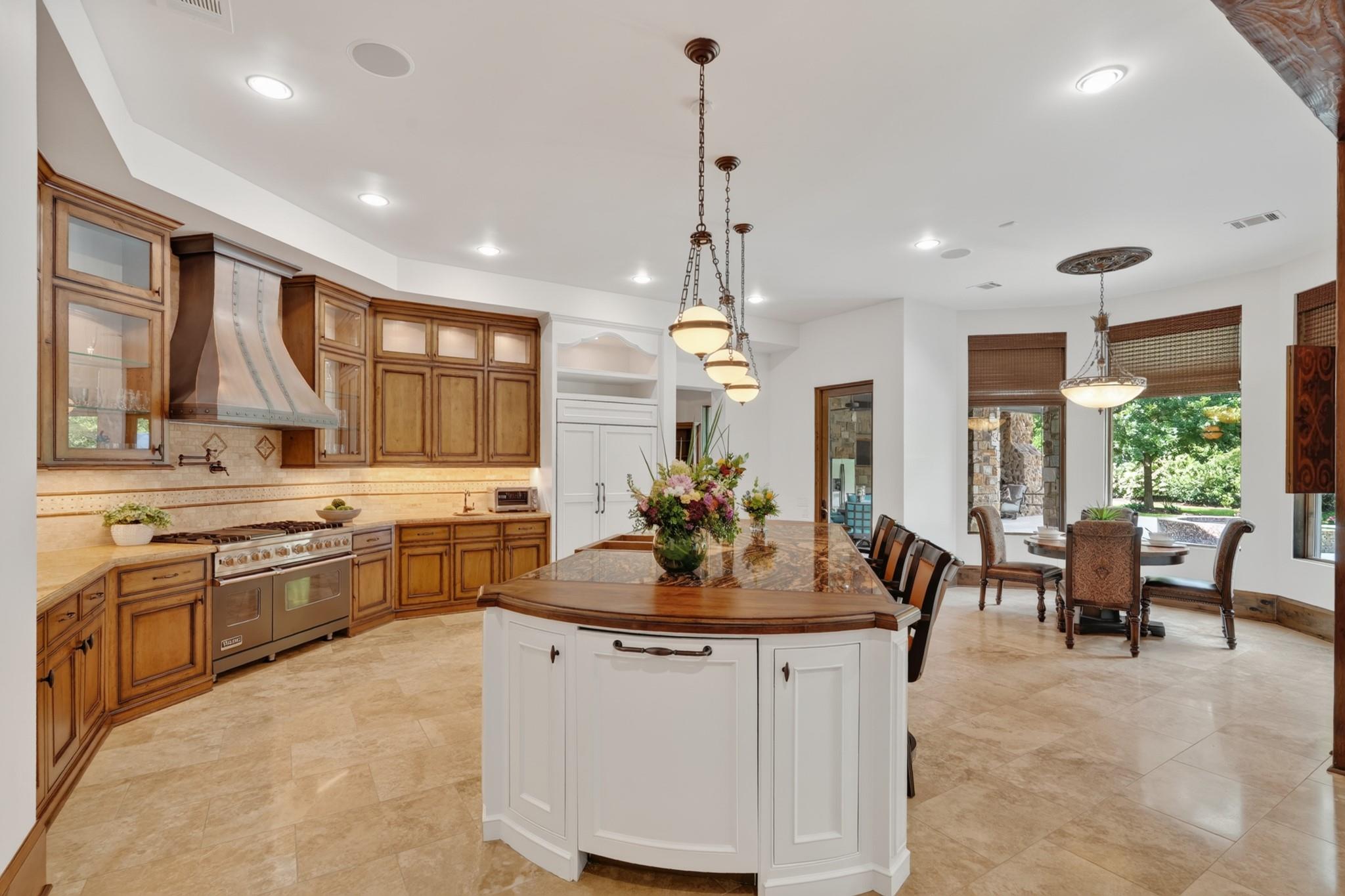 Kitchen with a large white island, warm wood cabinets, and an adjoining dining area opening to a leafy yard.