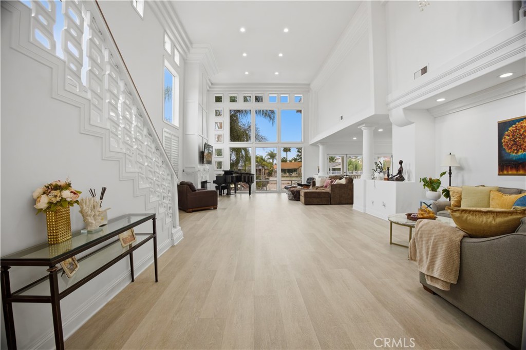 Double-height living room with a decorative staircase, tall windows, and a grand piano.