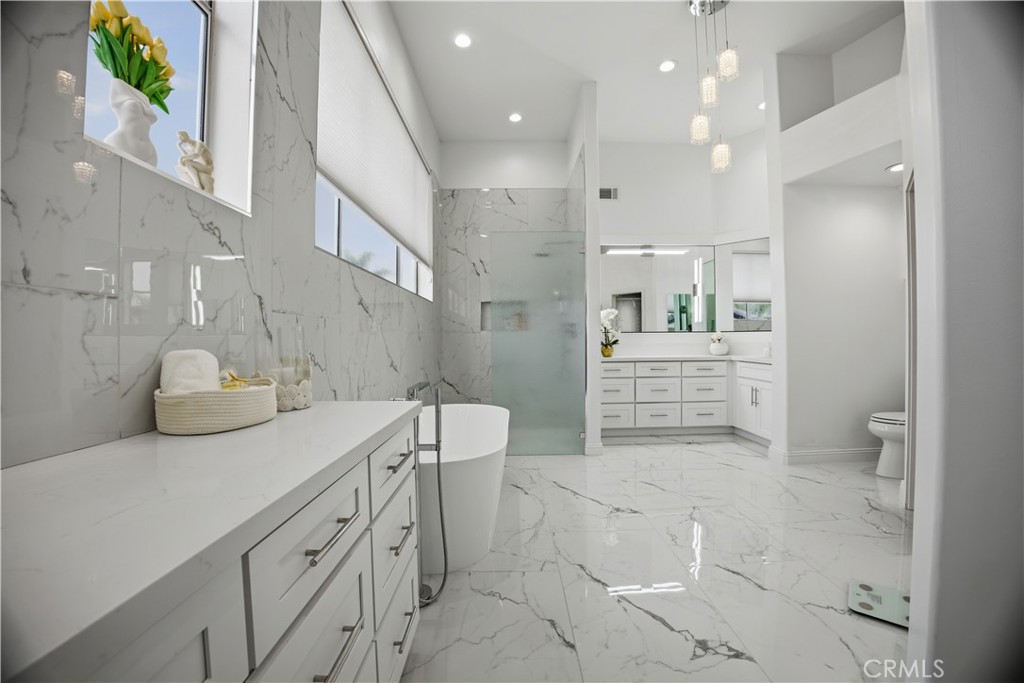Spacious white marble bathroom with glass shower, freestanding tub, and long vanity.