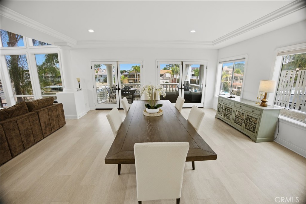 Bright dining room with a long wood table, white chairs, and large windows overlooking the water.