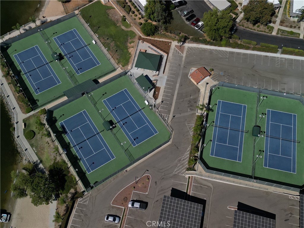 Aerial view of multiple fenced tennis courts beside a large parking area.