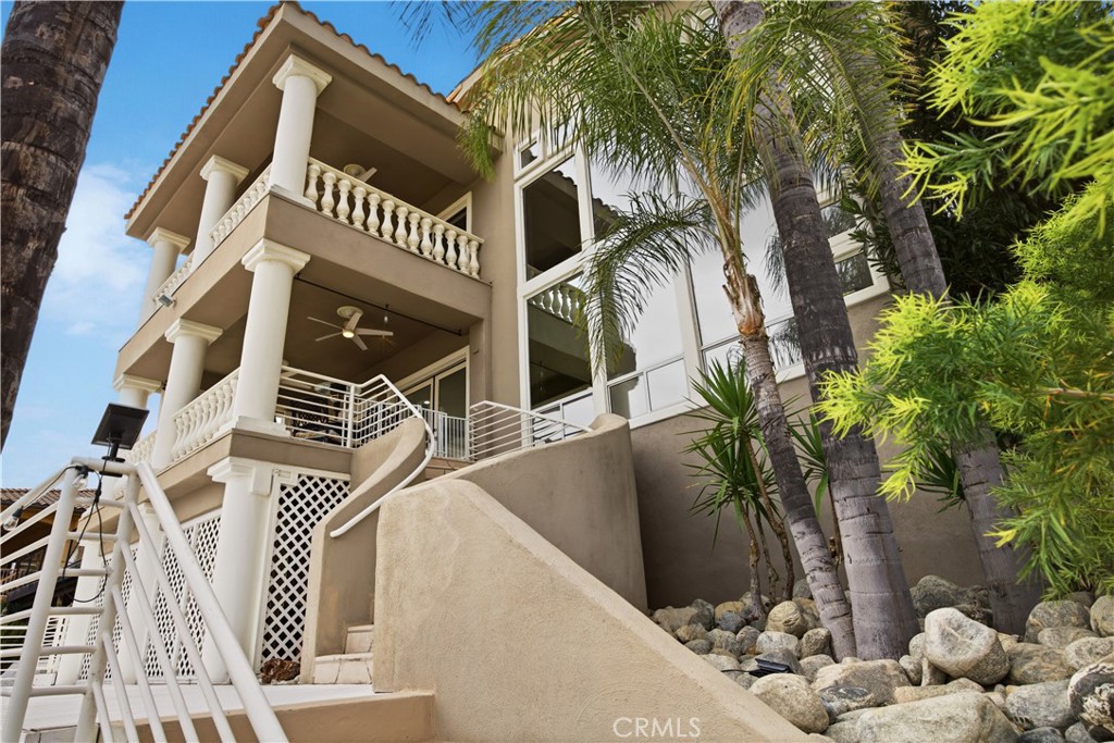 Multi-story beige home with columned balconies, a curved stairway, and palm trees.