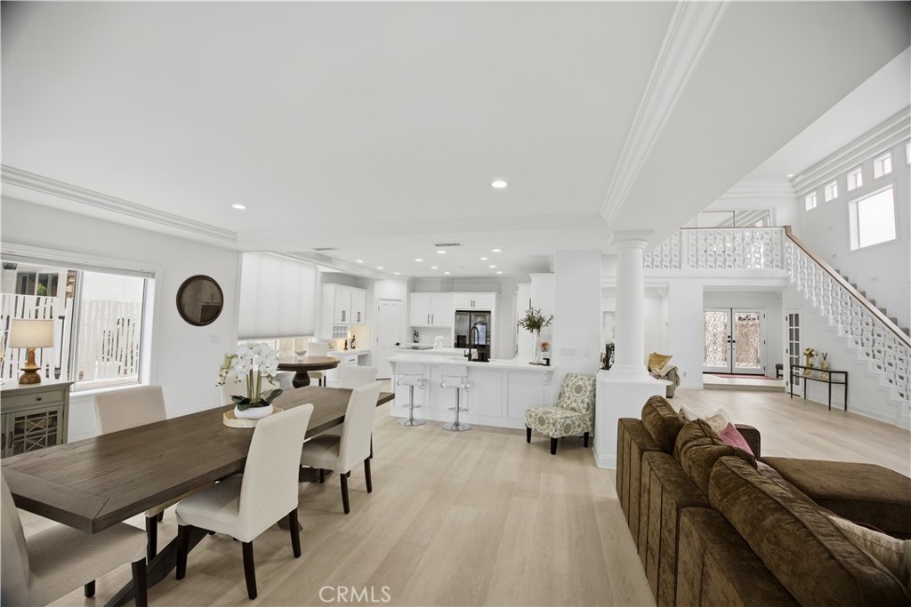 Open-plan living and dining area with a white kitchen, light wood floors, and an ornate staircase.