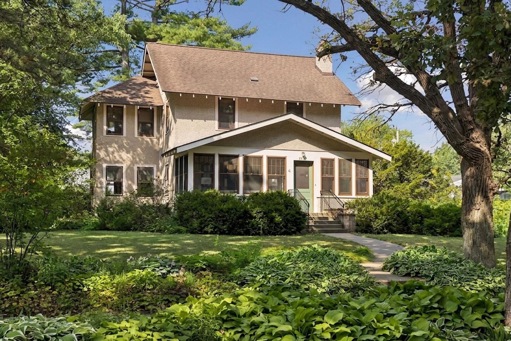 Two-story home with a glassed-in front porch, surrounded by mature trees and garden landscaping.