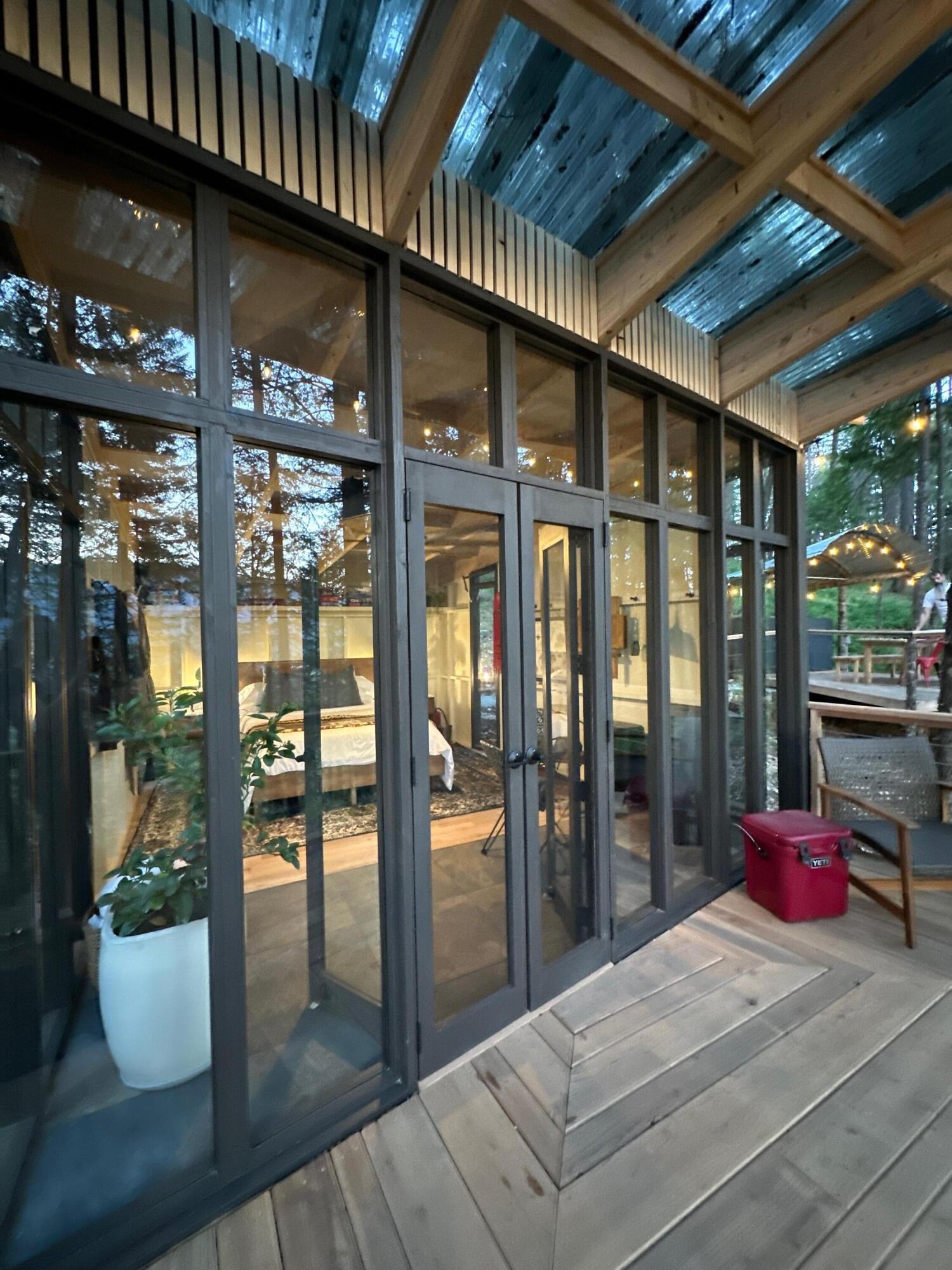 Modern cabin glass doors open onto a wooden deck, with a warmly lit bedroom visible inside.